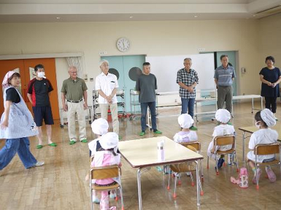 地域の方々が前に並び、調理帽姿の園児たちにあいさつをしている様子の写真