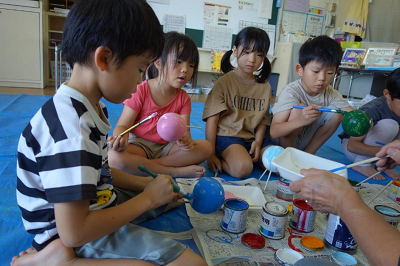 色とりどりの球体に絵の具を塗りながら真剣な表情で作業する園児たちの写真