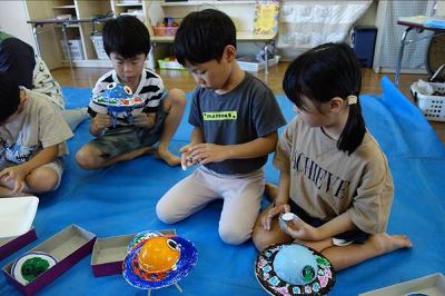 ビニールシートの上で園児たちが色を塗った紙皿と球体を組み合わせて作品を仕上げている写真