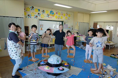 完成した立体作品を囲んで椅子の上に立った園児と先生がポーズをとっている写真