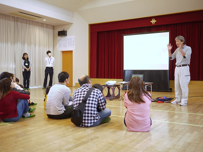 遊戯室で講師がスクリーンを使ってボッチャ体験会の説明をしている様子の写真