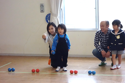 体育館で保護者に指示されながら幼児が青いボールを投げようとしている写真