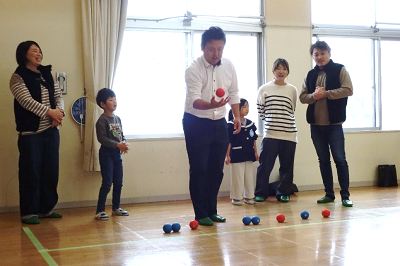 体育館でお父さんが赤いボールを構え子どもたちが並んで見守っている写真