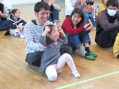 体育館で親子が床に座ってボッチャの試合を振り返りながら笑顔で拍手している写真