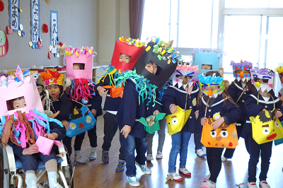 教室で園児たちがカラフルな鬼のお面をつけて集合写真を撮っている写真