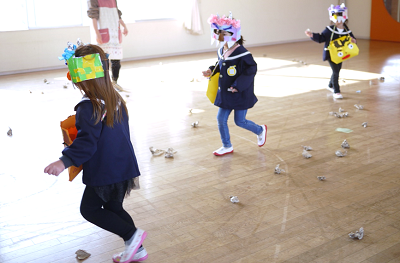 教室で園児たちが鬼のお面をつけて豆を拾いながら走っている写真