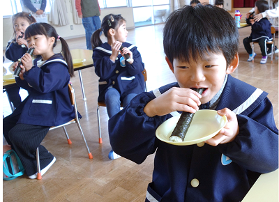 教室で園児たちが恵方巻を食べている写真