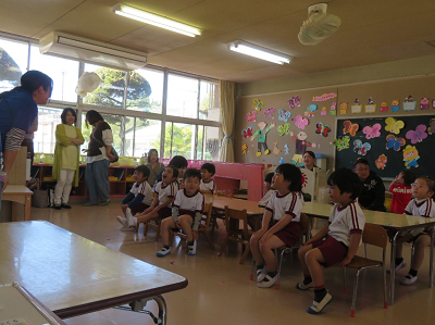 園児たちが教室で先生の話を聞きながら椅子に座っている写真