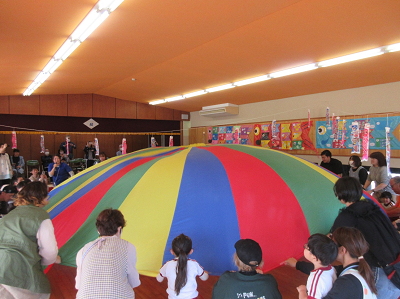 園児たちと保護者たちがカラフルなバルーンを大きく膨らませている写真