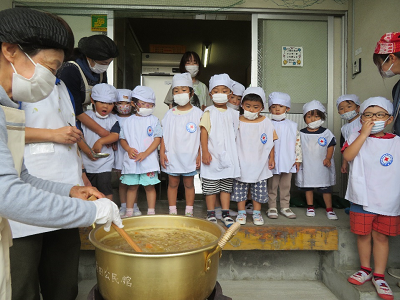 園児たちが大鍋で煮込まれているカレーをじっと見守っている写真