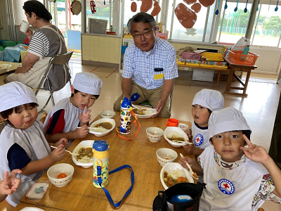 男性一人と園児4人が椅子に座って楽しそうにカレーを食べている様子の写真