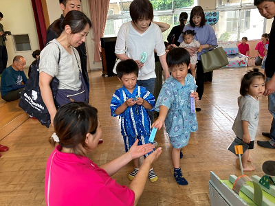 室内の会場で浴衣姿の子どもたちが受付の職員にチケットを渡している写真