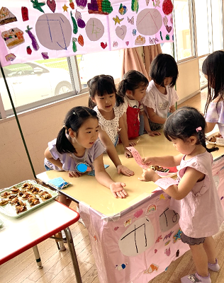 室内の模擬店コーナーで子どもたちがカウンター越しにやりとりをしている写真