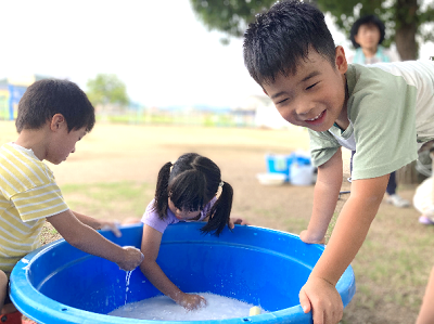 たらいの水や泡に手を入れて遊ぶ子どもたちと笑顔でのぞき込む男の子の写真