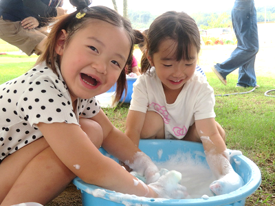 泡だらけの手でたらい遊びをしながらにこにこ笑っている女の子たちの写真