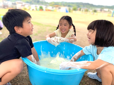 泡の入ったたらいを囲んで楽しそうにおしゃべりしながら遊ぶ子どもたちの写真