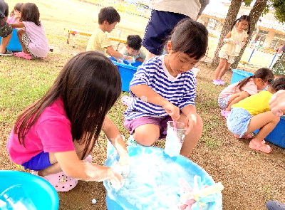 たらいの泡をカップに入れながら真剣な表情で遊んでいる女の子たちの写真