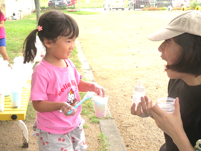 泡の入ったカップを見せる女の子と驚いた表情で応える保育者の写真