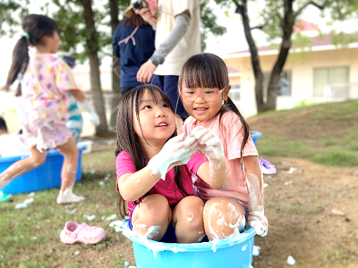 青いたらいの中で泡まみれになりながら寄り添って笑っている女の子たちの写真