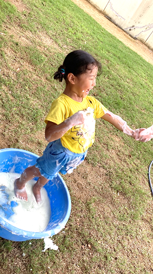 泡の入ったたらいに足を入れて手をつないでもらいながらうれしそうに立っている女の子の写真