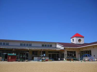 青空の下、ひときわ赤い三角屋根とカラフルな遊具が設置されている寒川幼稚園の写真