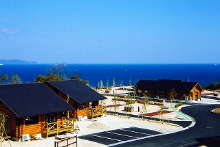 雲一つ無い青空が広がる海に面した場所に3棟のコテージが建てられている写真
