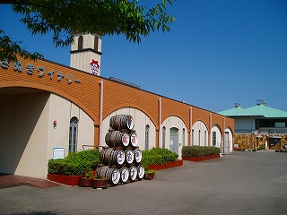 茶色いアーチ状の壁模様がある大きな建物の前に樽がピラミッド状に積み重ねられている写真