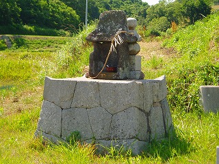 芝生の上に小さな石垣があってその上に小さな祠が置かれている写真