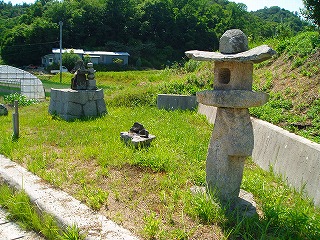 奥に小さな祠が見える芝生の上に置かれた灯籠の写真