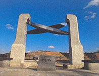 奥に山の見える場所に建てられた石造りのモニュメントの写真