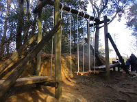 ロープに繋がれた丸太が垂れ下がったアスレチックの写真