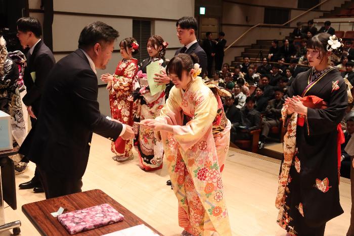 壇上で恩師から参加者が抽選会の景品を受け取っている写真