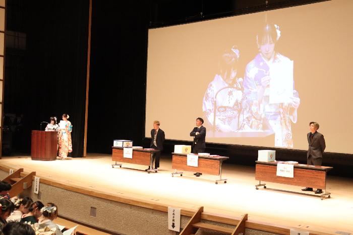 式典に参加している参加者が壇上で抽選会の進行の仕方を説明している写真