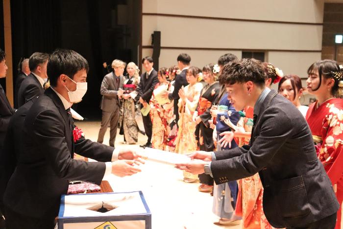 式典の参加者が壇上で笑顔で景品を受け取っている写真