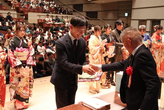 式典の参加者が壇上で笑顔で恩師と握手している写真