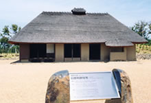 手前に定礎板のある茅葺き屋根の平屋の建物の写真