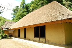 土の上に建てられた茅葺き屋根の平屋の建物の写真