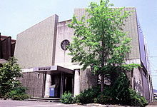 手前に木がある鉄筋コンクリートの建物の写真