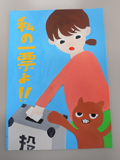 投票をする女性に手を伸ばそうとしている茶色いキャラクターの隣に「私の一票よ！！」と書かれた紙の写真