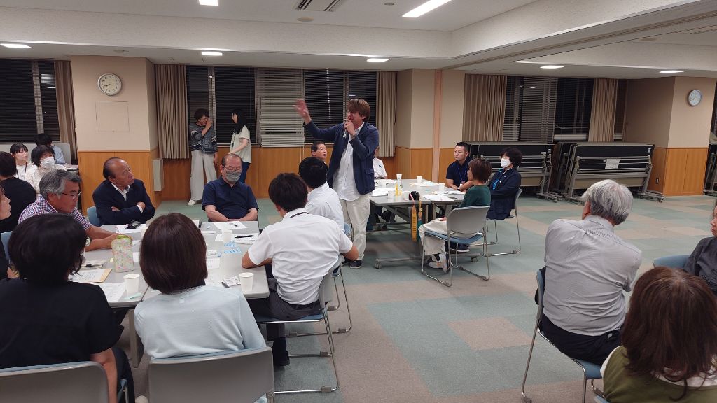 立って話す男性の意見を聞いている複数のグループの写真