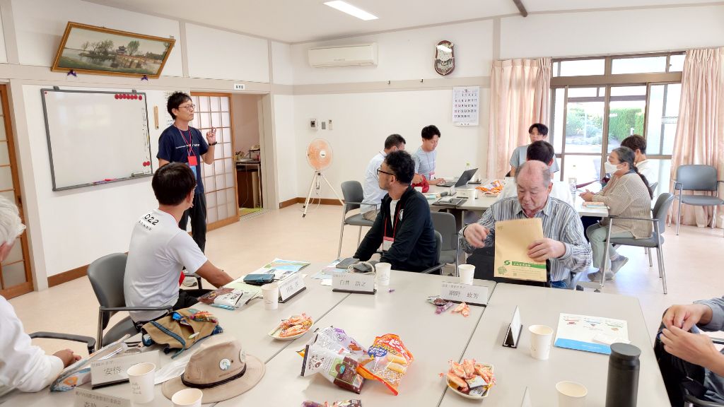 集会所で参加者がテーブルを囲んで話を聞いている写真