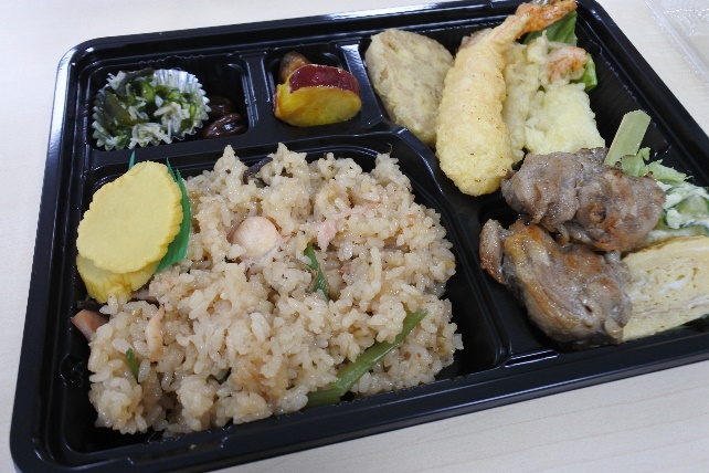 炊き込みご飯と天ぷらなどのおかずが入った弁当の写真