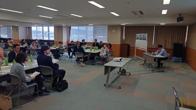 会議室でテーブルに分かれて着席した参加者たちが講師の話を聞いている写真