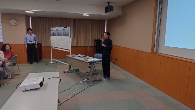 会議室の前方でマイクを持った女性講師が立って話している写真