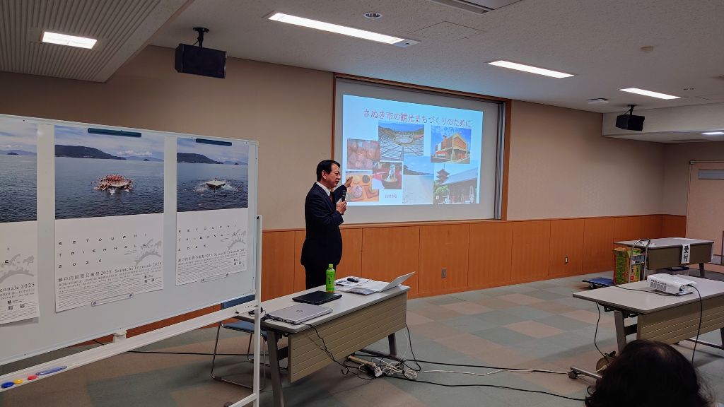 会議室でスクリーンと展示パネルを前にスーツ姿の男性講師が説明をしている写真