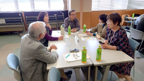 会議室のテーブルを囲んで中高年の参加者たちが話し合いをしている写真