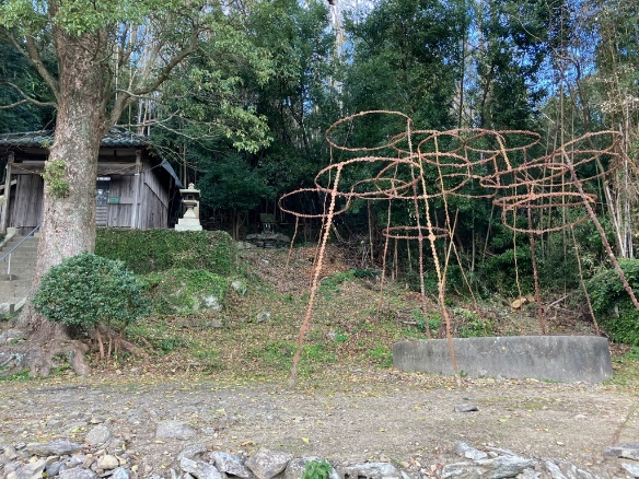 森林の前に立つ古い建物と金属のオブジェが並ぶ風景写真