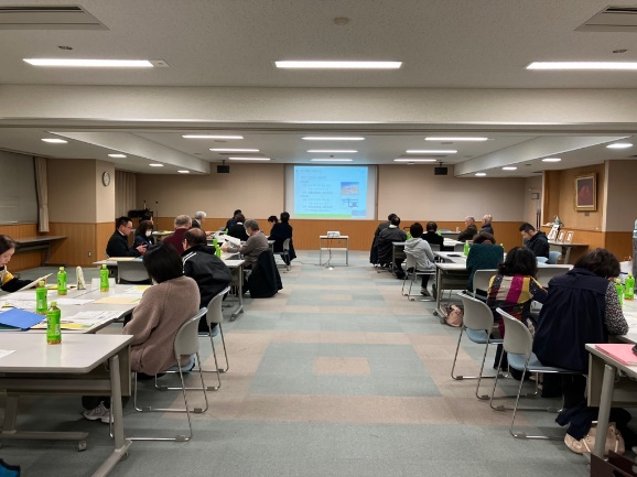 会議室で参加者たちが前方のスクリーンを見ながら資料を読み進めている写真