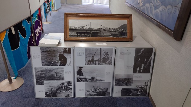 展示台の上に昔の漁の様子を写した白黒写真パネルと長いパノラマ写真がまとめて展示されている写真