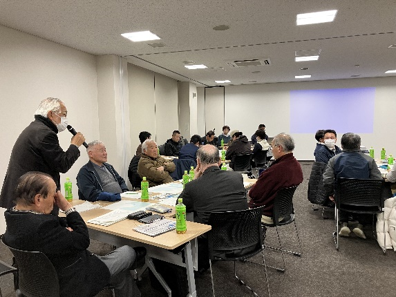 参加者の男性がマイクを持って発言し、周囲の参加者が聞いている写真